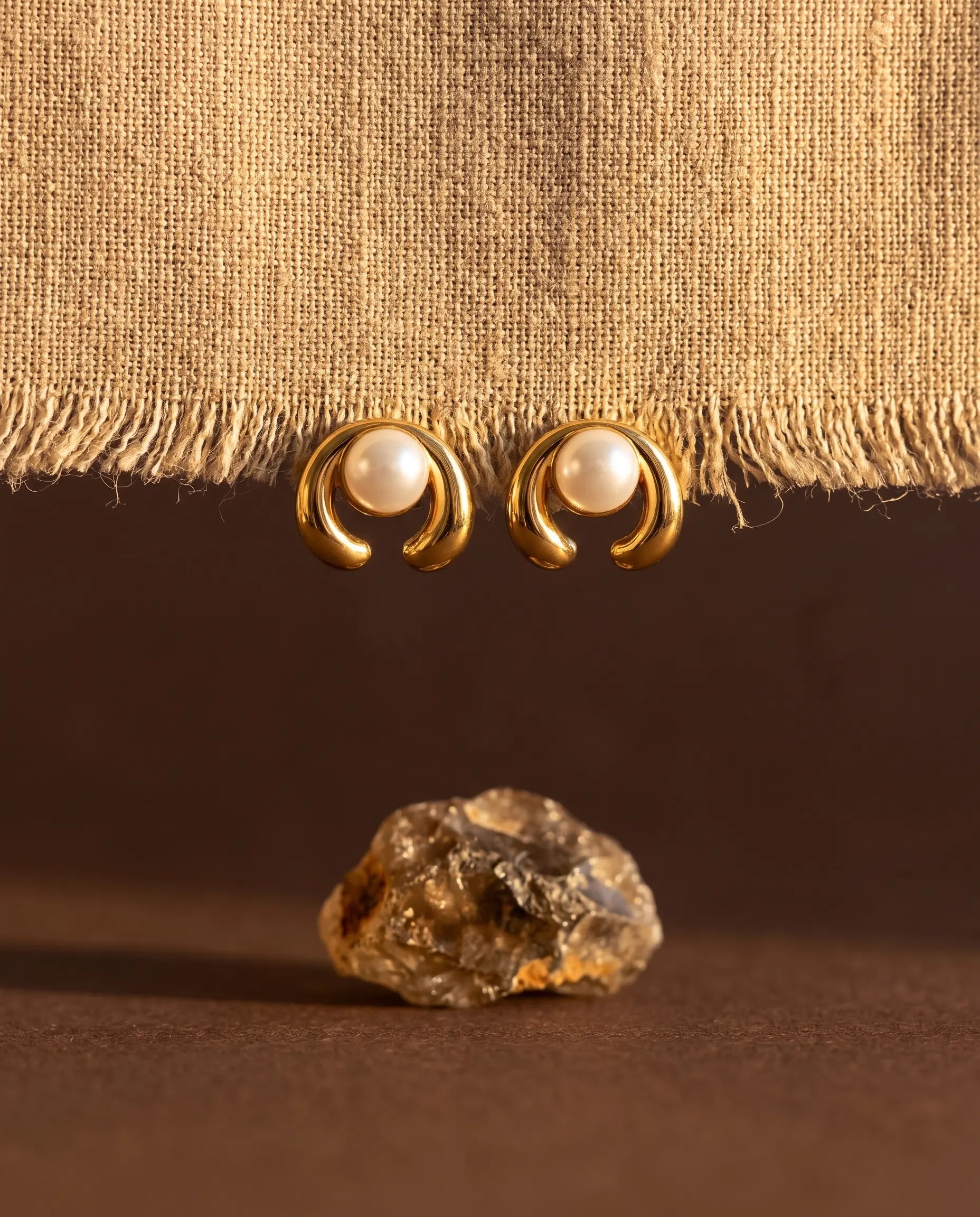 celine-pearl-arch-studs-displayed-on-natural-texture-highlighting-the-sophisticated-arch-silhouette-and-finish