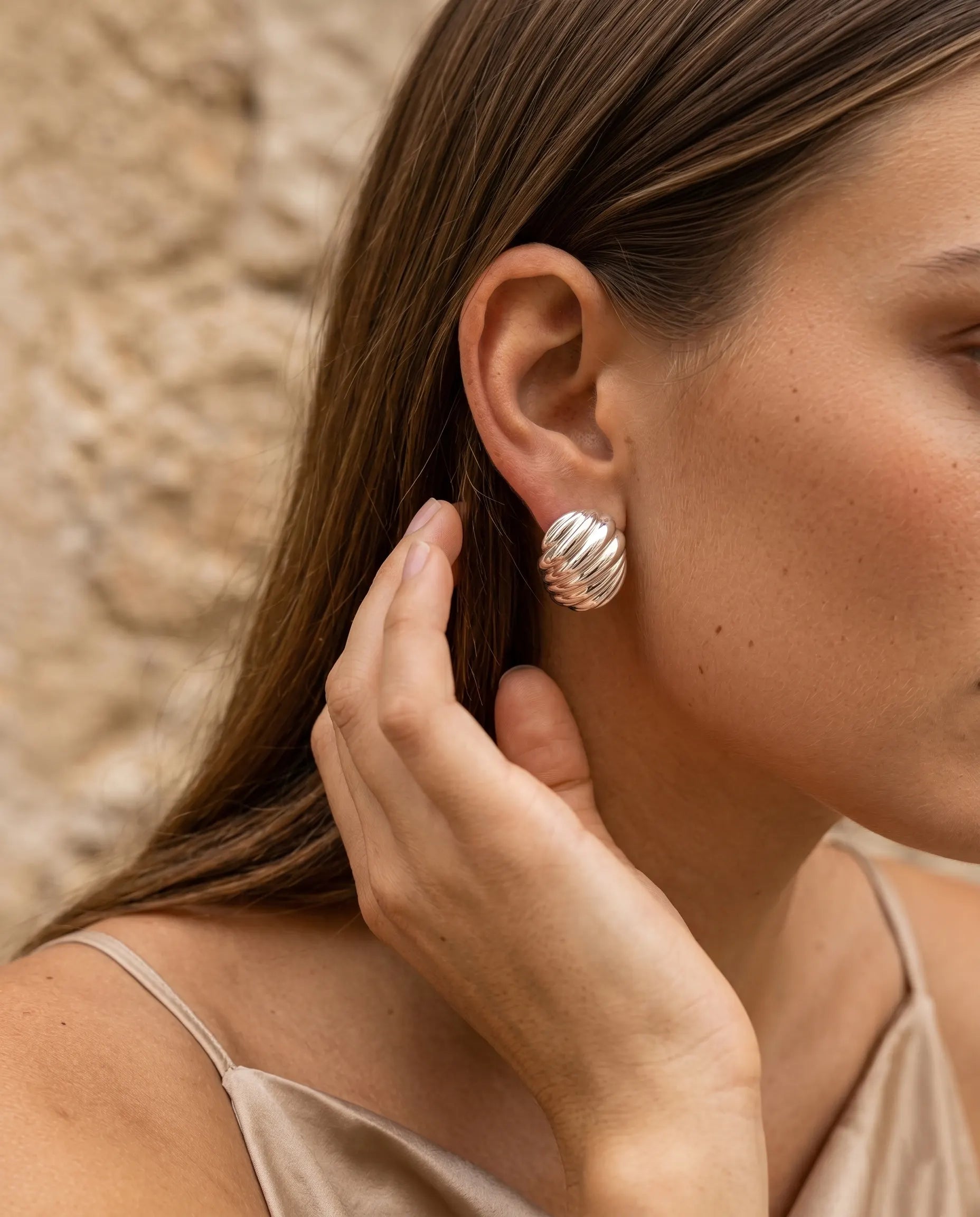 model-putting-on-gold-nia-ribbed-stud-earrings-lifestyle, elegant-modern-feminine-jewelry-on-ear, professional-women-luxury-accessories, chic-textured-gold-styling, luxury-lifestyle-brand-model