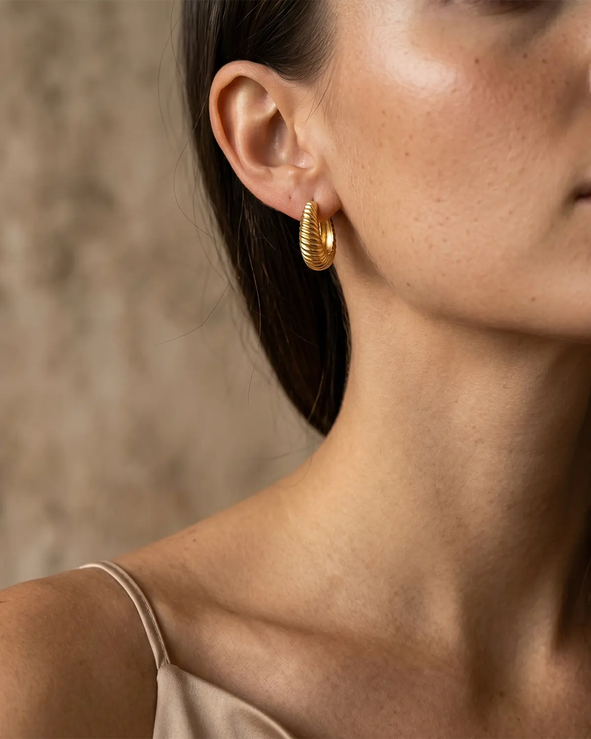 model-wearing-the-sloane-ribbed-huggie-hoops-showcasing-sophisticated-minimalist-ear-stacking-styling, textured-sterling-silver-huggie-hoops-captured-in-warm-natural-light-to-emphasize-the-rhythmic-ribbed-surface