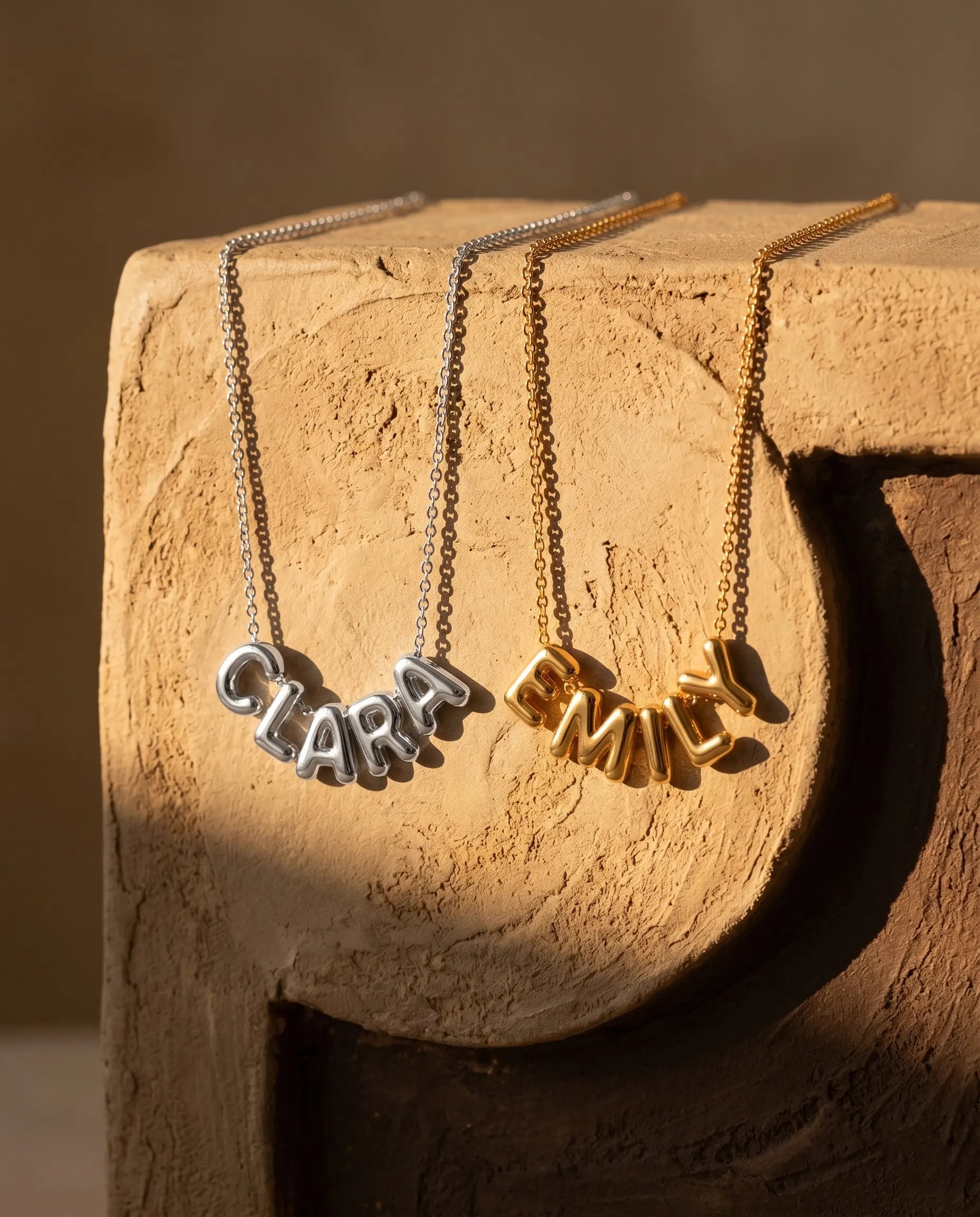 poppy-custom-name-necklaces-draped-over-natural-stone-display-showcasing-the-durable-chain-and-script