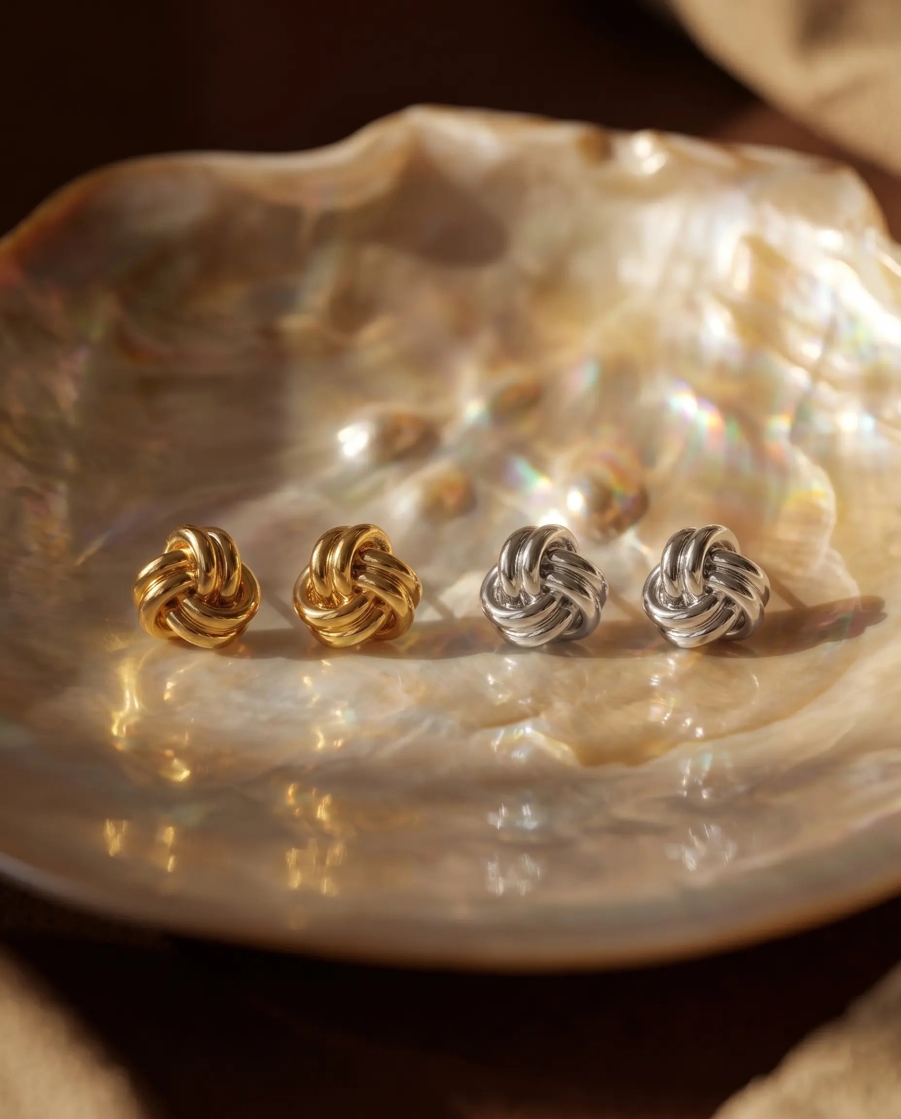timeless-knot-design-earrings-gold-silver-mix, artistic-jewelry-photography-shadows, gift-ideas-for-women-silver-earrings, small-knot-studs-high-shine-finish, polished-925-silver-studs-premium, refined-jewelry-collection-germany