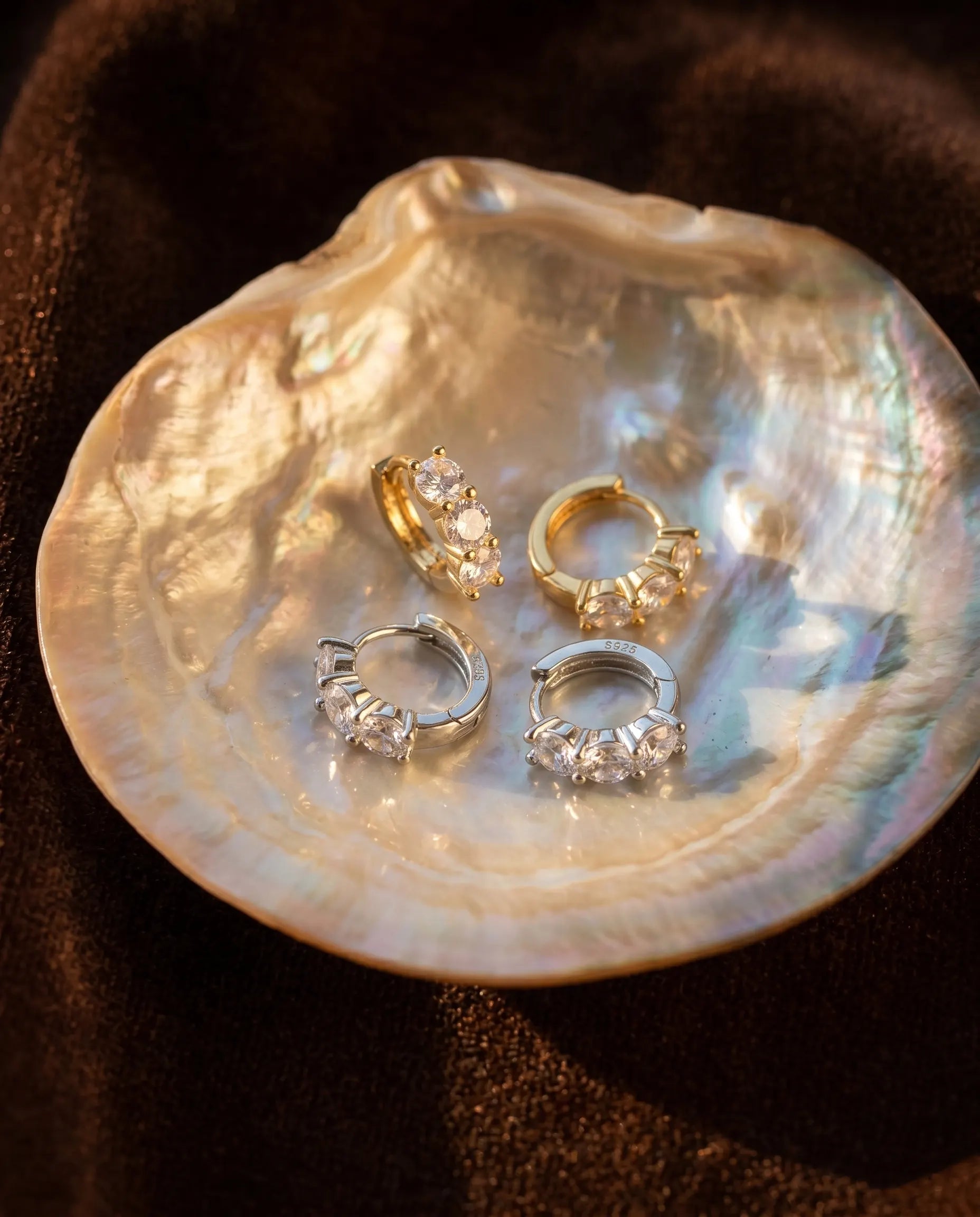 artistic-jewelry-display-blanca-huggie-earrings-silver-gold, creative-still-life-luxury-accessories-lighting, premium-fine-jewelry-showcase, modern-radiant-hoop-presentation