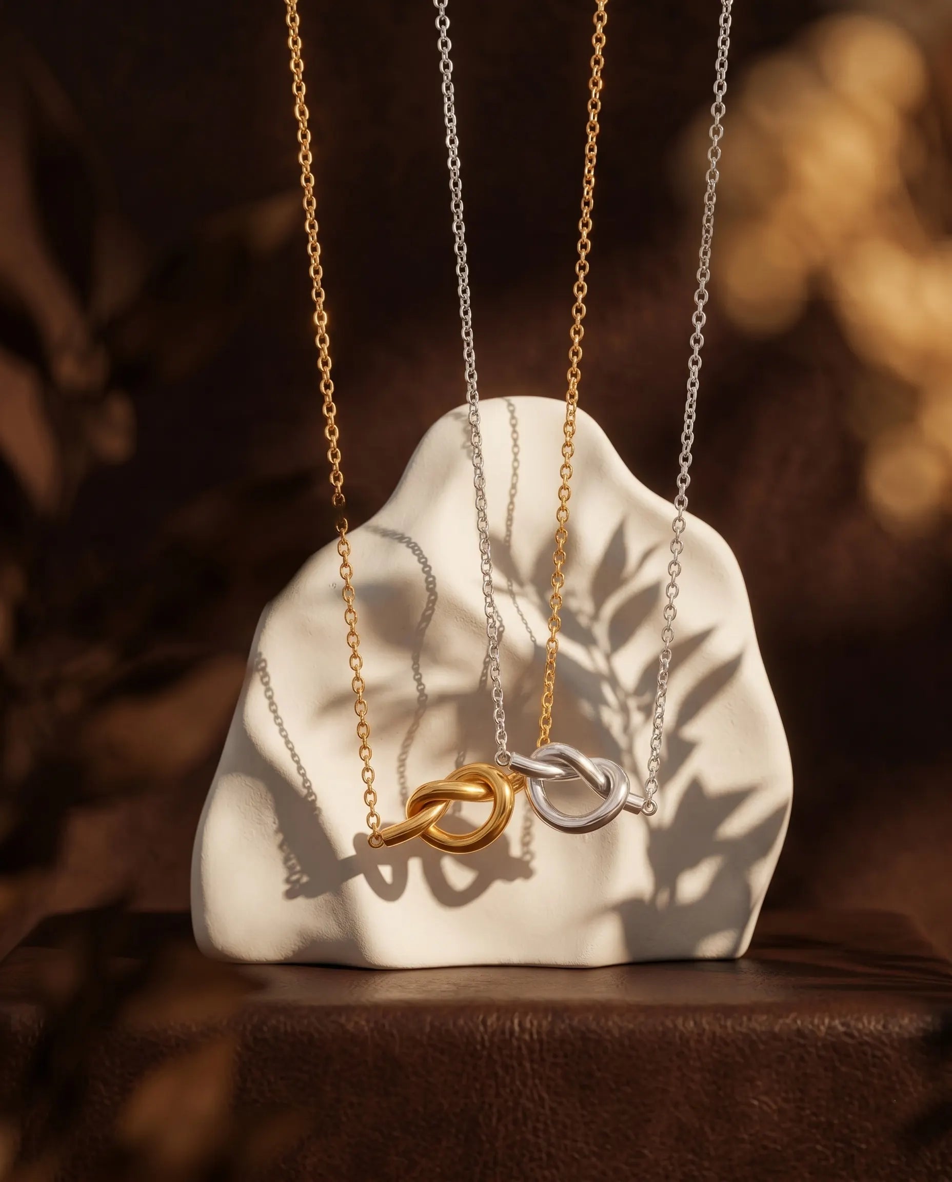 nerissa-knot-necklace-in-gold-and-silver-on-textured-background-minimalist-jewelry-photography-for-senya