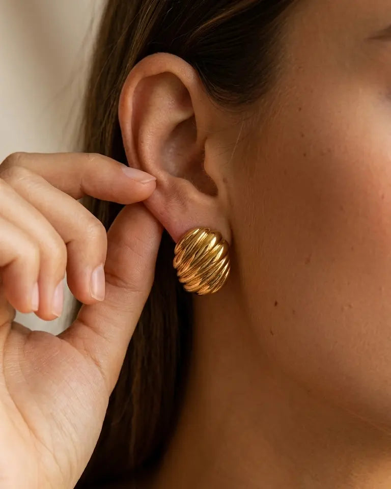 model-putting-on-gold-nia-ribbed-stud-earrings-lifestyle, elegant-modern-feminine-jewelry-on-ear, professional-women-luxury-accessories, chic-textured-gold-styling, luxury-lifestyle-brand-model