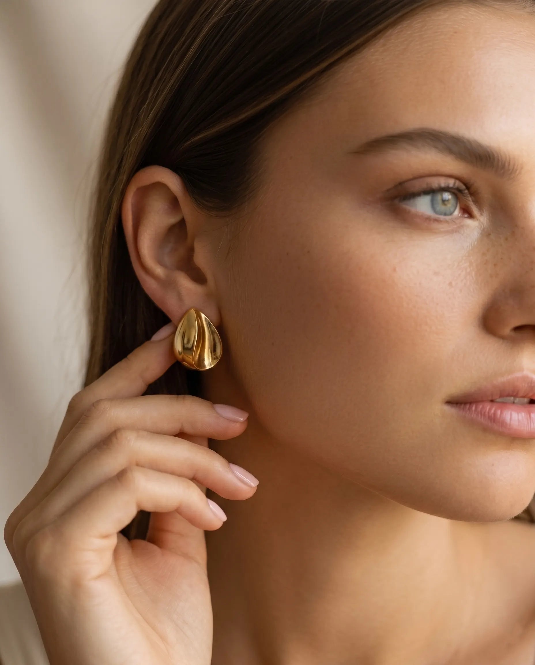 model-wearing-gold-rhea-teardrop-studs-lifestyle, elegant-modern-bold-jewelry-on-ear, professional-women-luxury-accessories, chic-gold-organic-earring-styling, luxury-lifestyle-brand-model