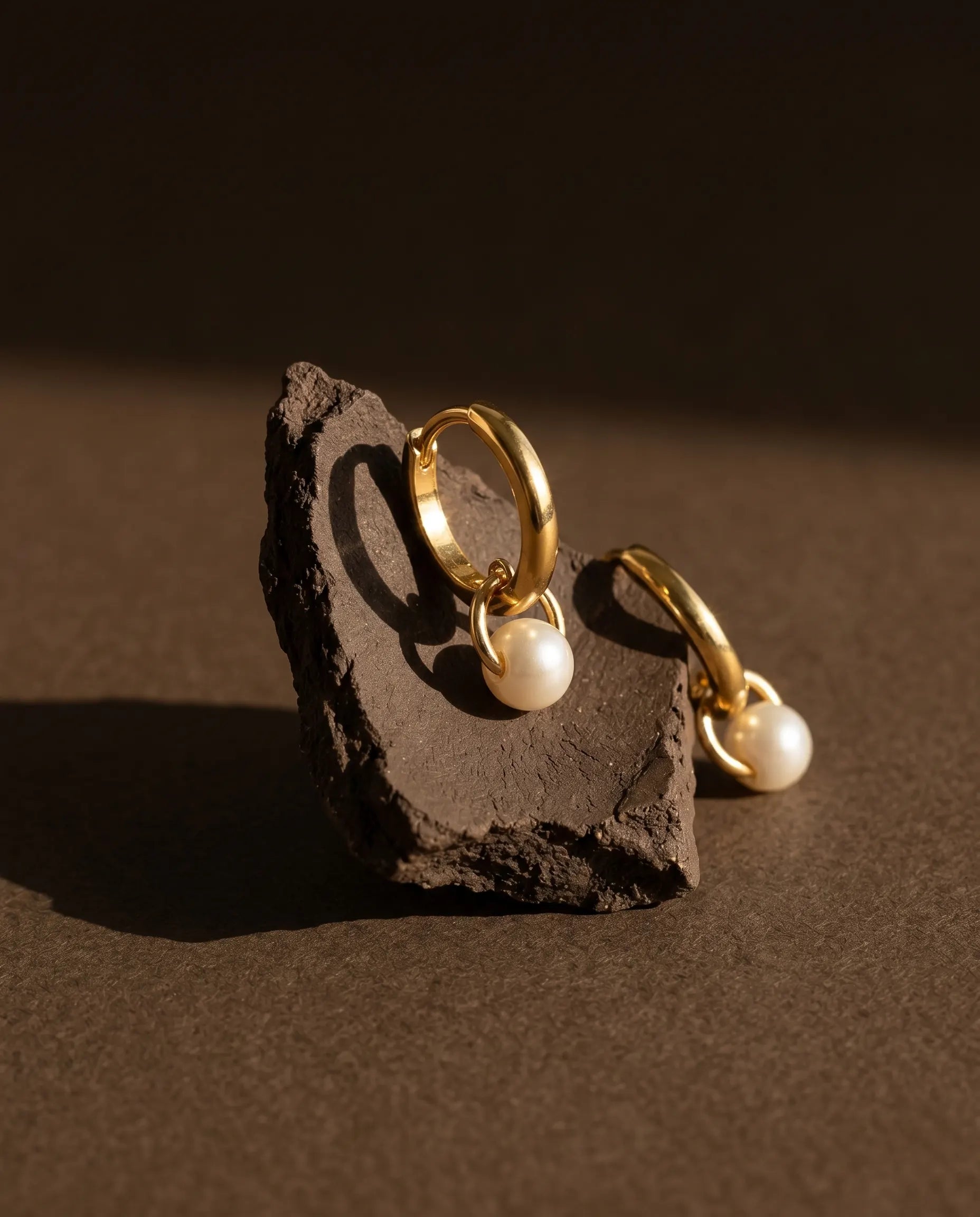 palma-pearl-drop-huggie-hoops-on-rústic-stone-highlighting-the-organic-pearl-luster-and-sterling-silver-quality